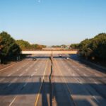 An empty highway in Houston, Texas, featuring autumn-colored trees and a clear sky.