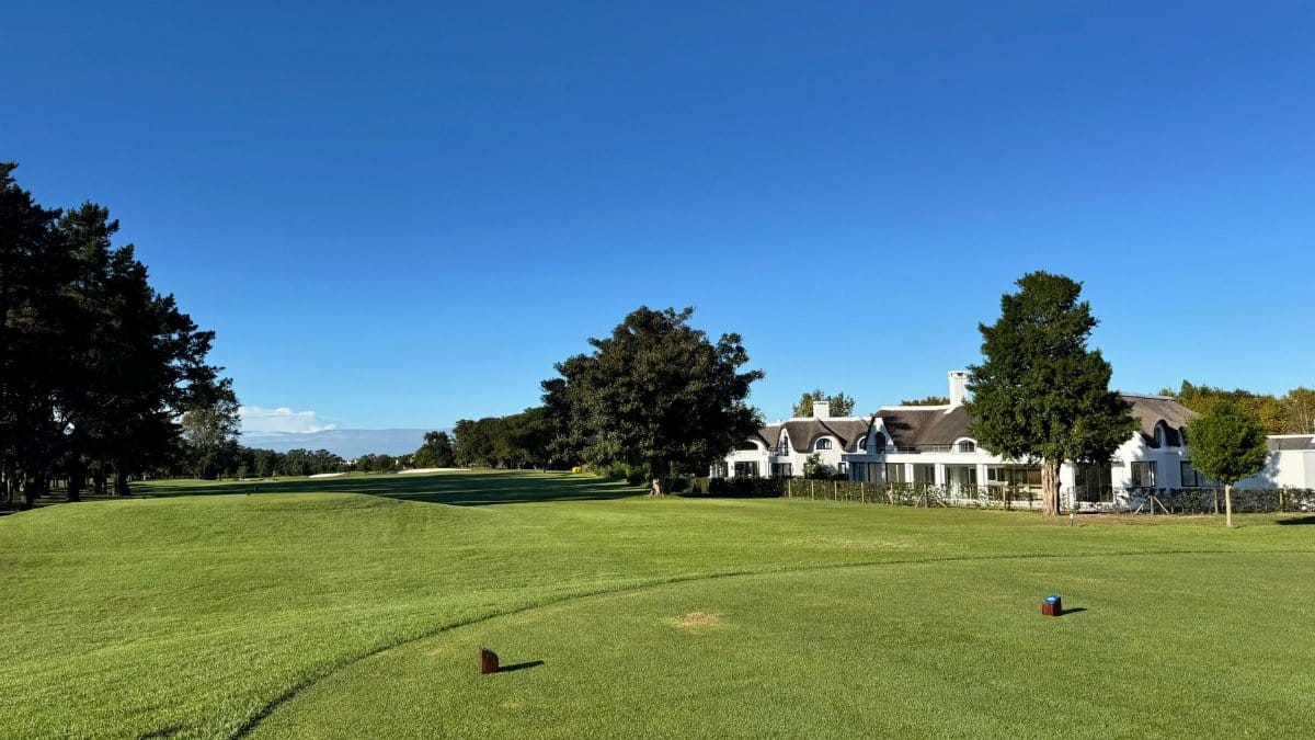 A picturesque view of a golf course fairway with a clubhouse and lush greenery under a clear blue sky.