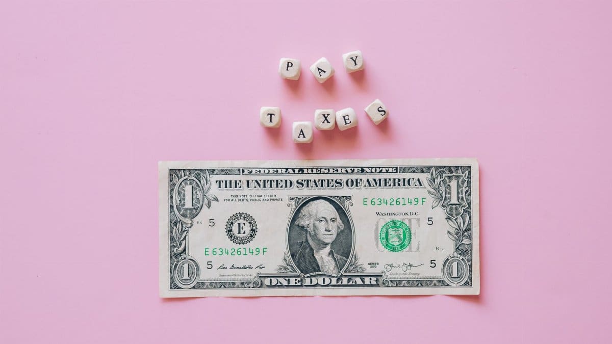 US one dollar bill on a pink background with pay taxes reminder cubes.