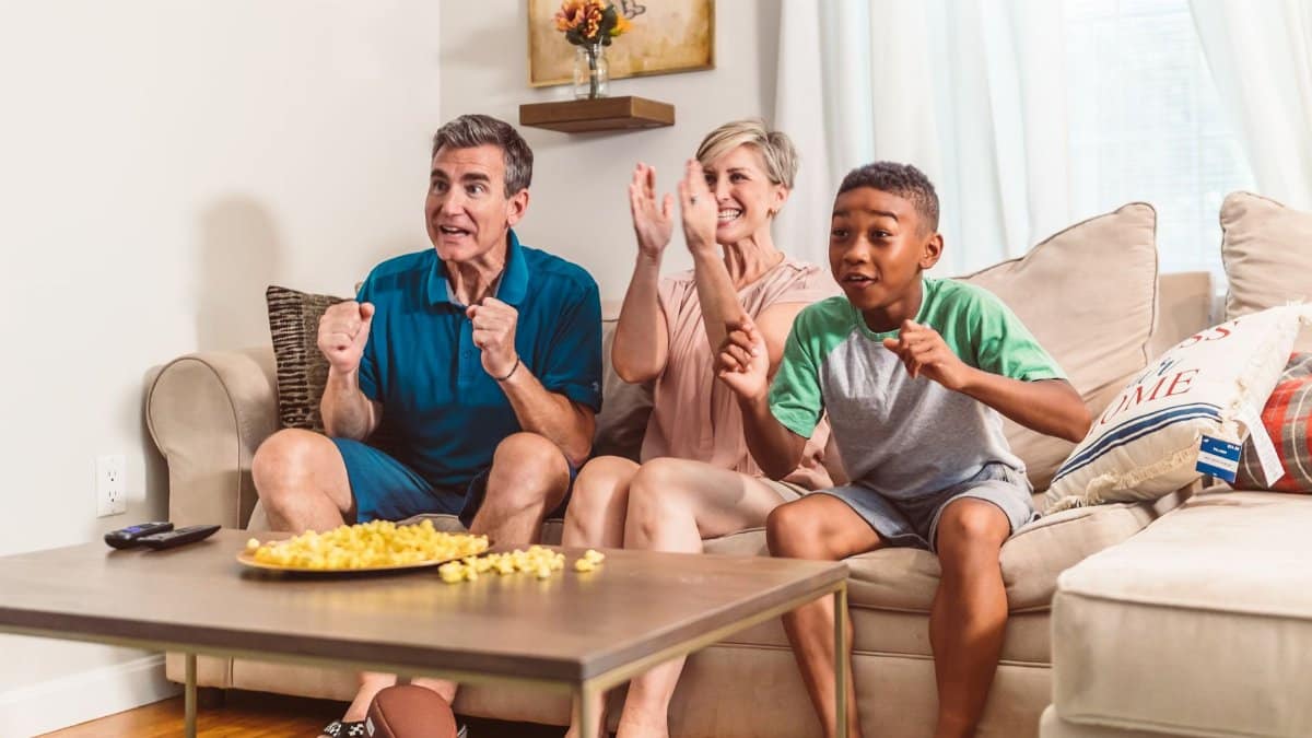 A joyful family bonding experience while watching TV and enjoying snacks on the sofa.