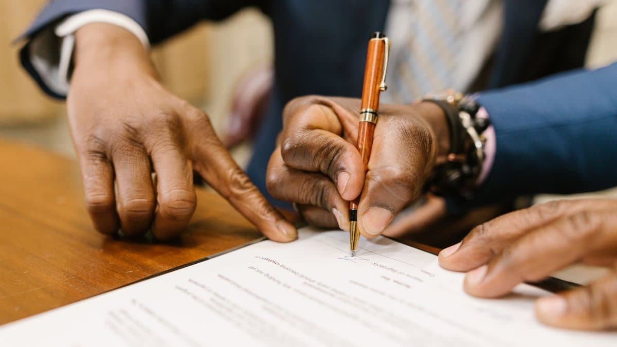 Close-up of business professionals signing a legal contract in an office setting.