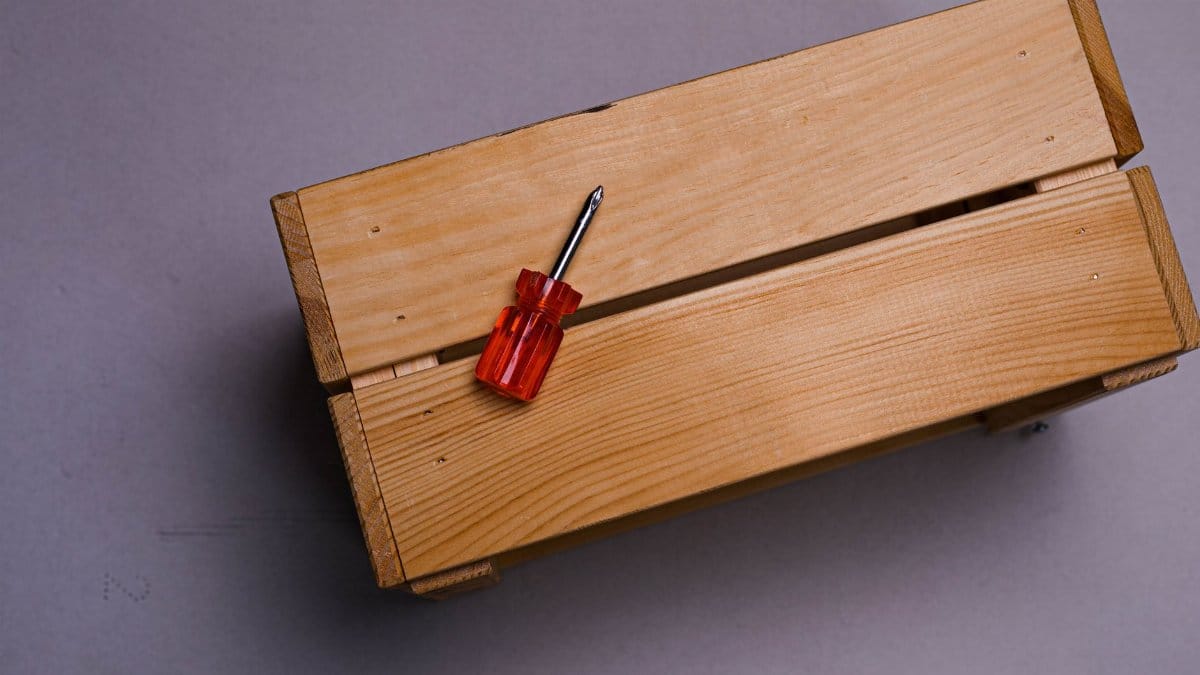 Top-down view of a wooden box with a red screwdriver on a grey background, emphasizing simplicity and utility.
