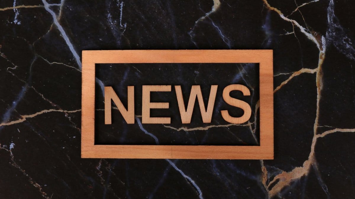 Wooden text of 'news' outlined on a dark, marbled surface, creating a striking contrast.