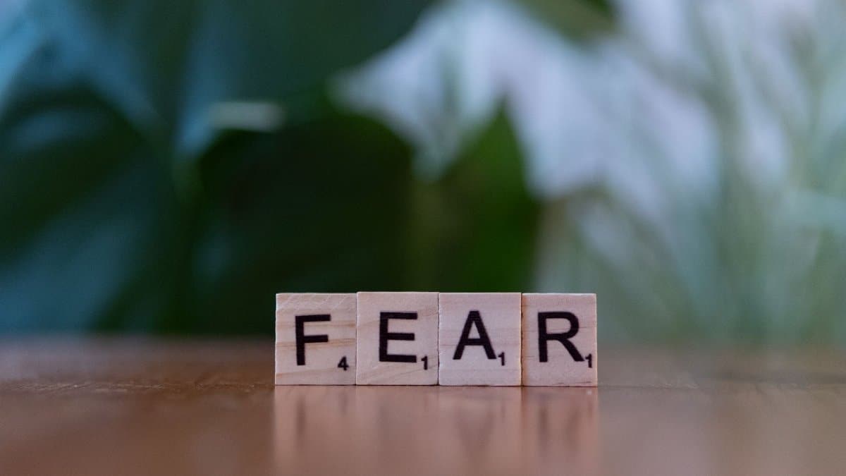 Wooden letter blocks spelling 'FEAR' on table against blurred green background. Emphasizes emotion and challenge.