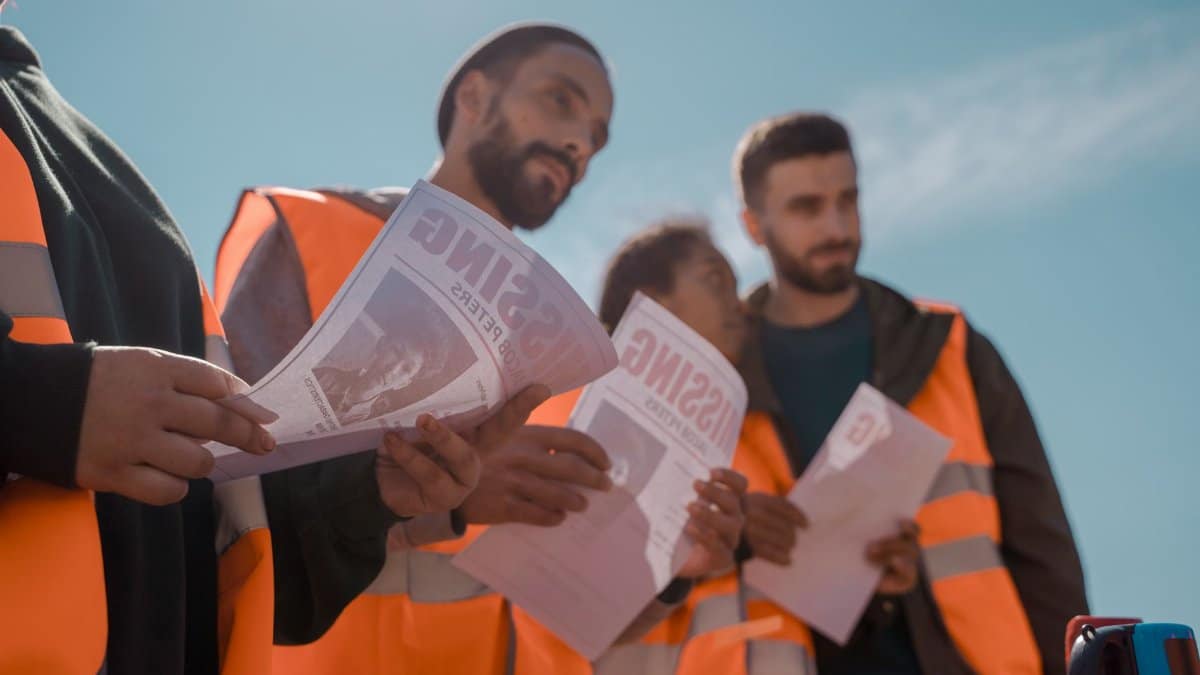 Group of volunteers in orange vests distributing missing person flyers outdoors.