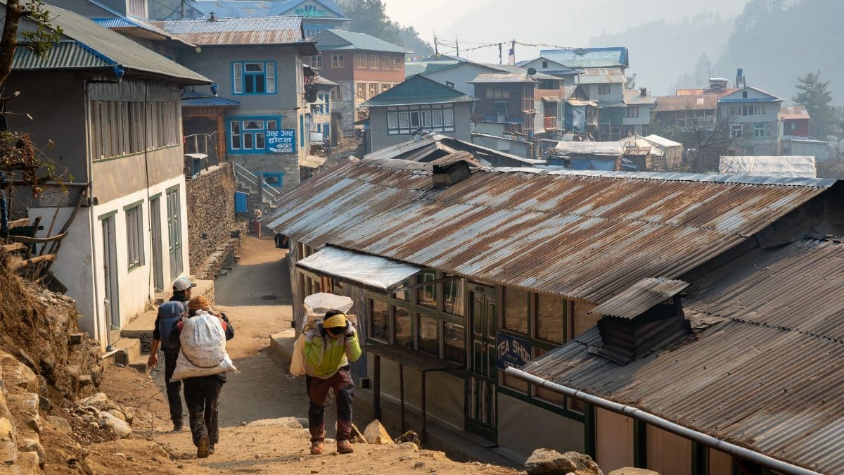 Villagers carrying loads on a rustic pathway in Himalayan village setting.