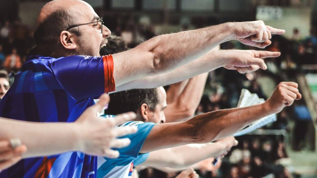 Energized sports fans pointing and cheering during a thrilling match in a stadium.