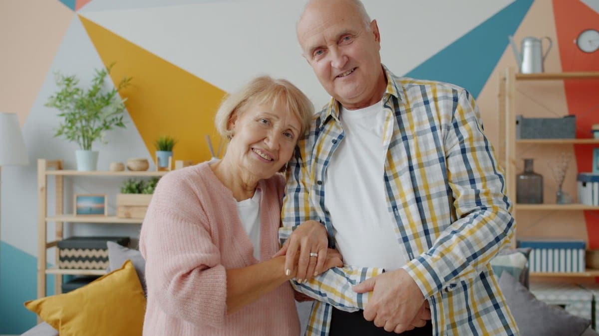Elderly couple smiling warmly in a modern, vibrant living room setting.