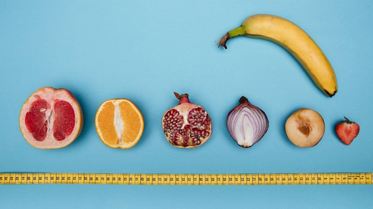 Fruits arranged with a measuring tape on a blue surface, symbolizing size and sexuality.