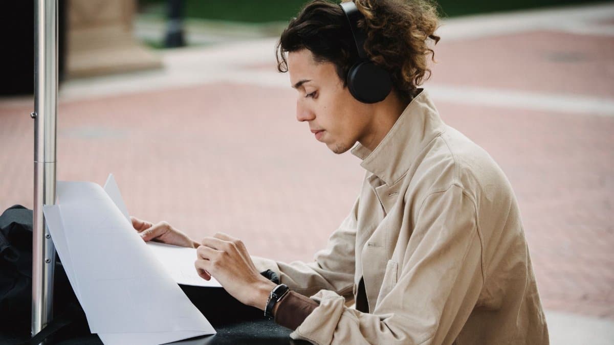 Side view of concentrated male learner preparing report for university assignment while listening to music in wireless headphones