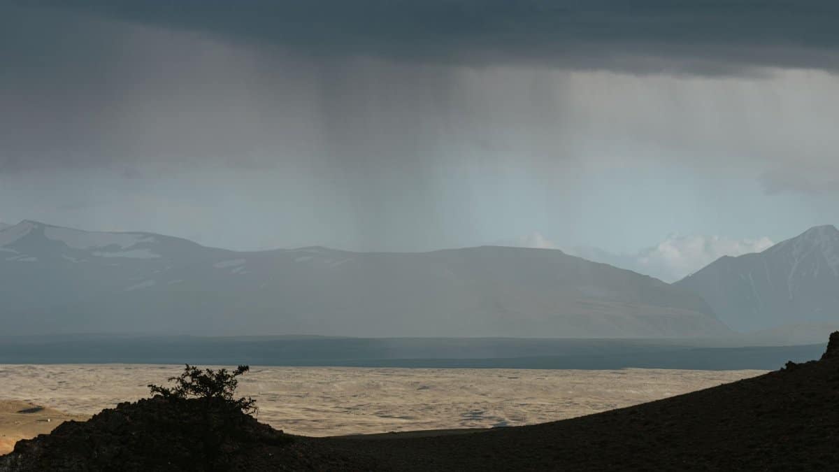 Dramatic scene of mountains and rainfall under a gloomy sky, capturing nature's raw beauty.