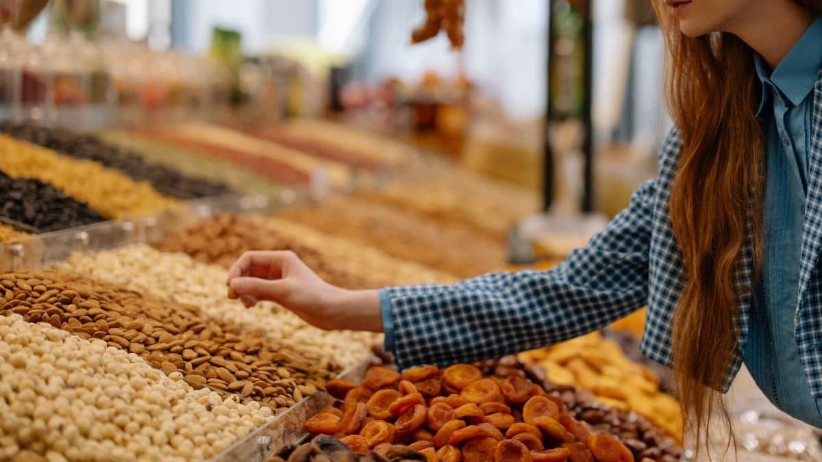 A woman is choosing a variety of nuts at an outdoor market stall, showcasing vibrant colors and textures.