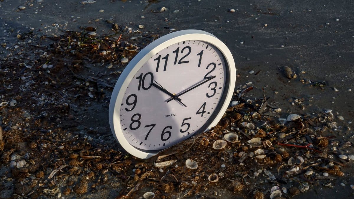 Analog clock on a sandy, shell-covered beach. Concept of time and nature.