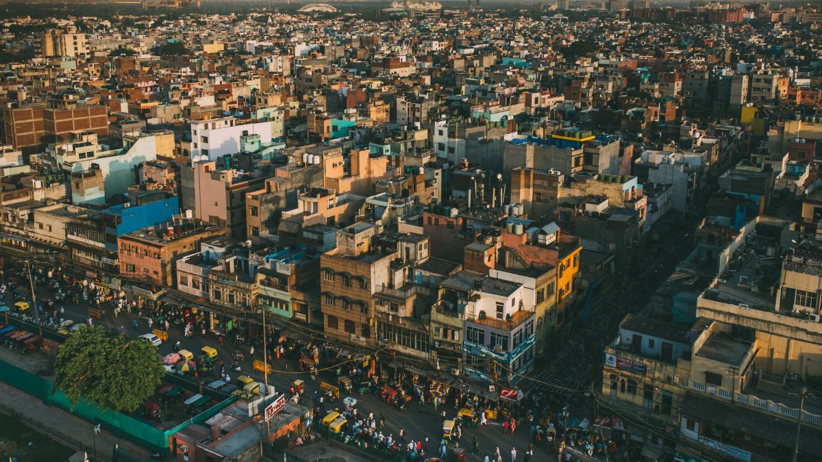 A vibrant aerial cityscape of Delhi, showcasing the bustling streets and diverse architecture under warm daylight.