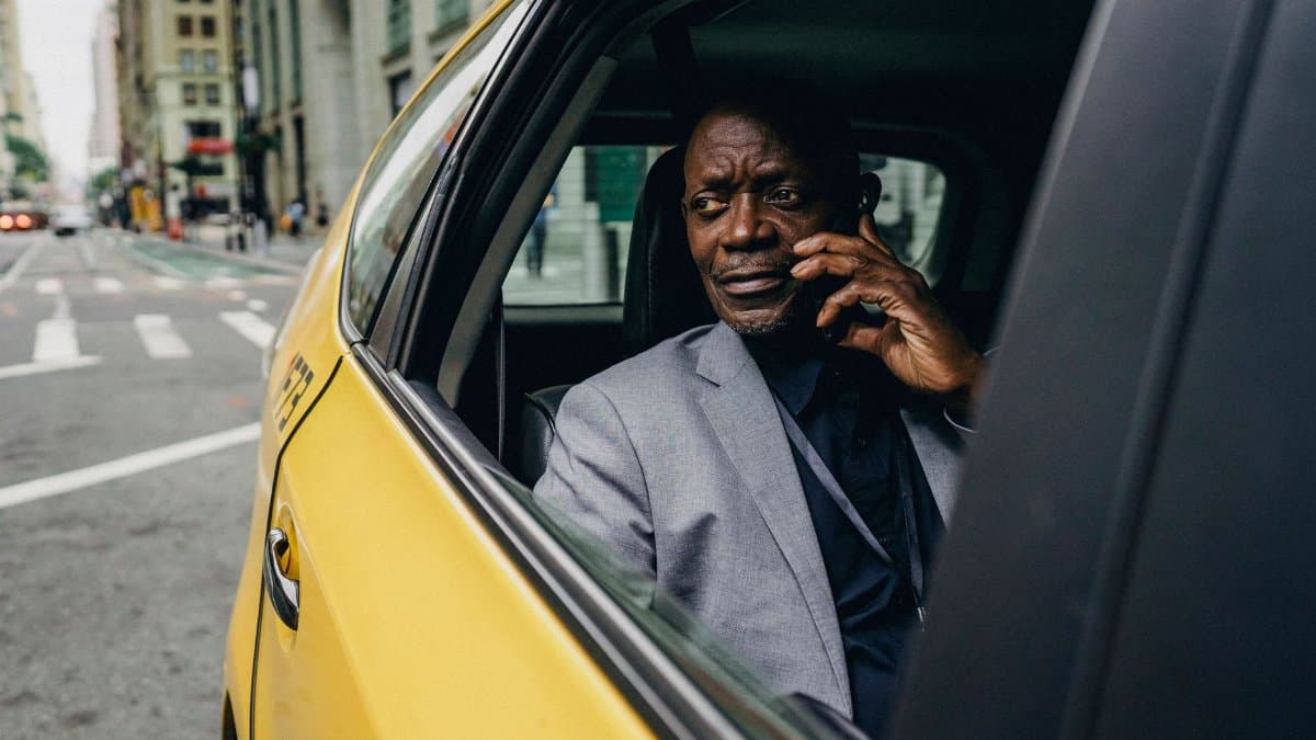 Serious African American male in formal clothes riding taxi on passenger seat and having conversation on mobile phone