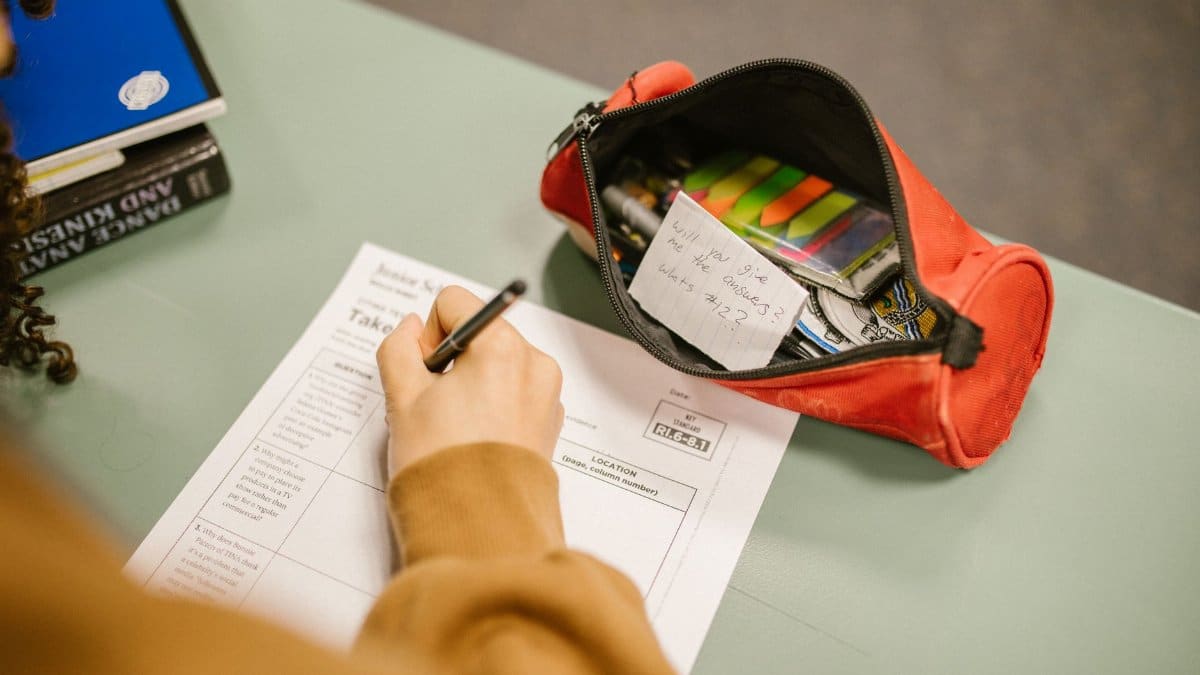 A college student using cheat notes during an exam with visible test paper and pencil case.