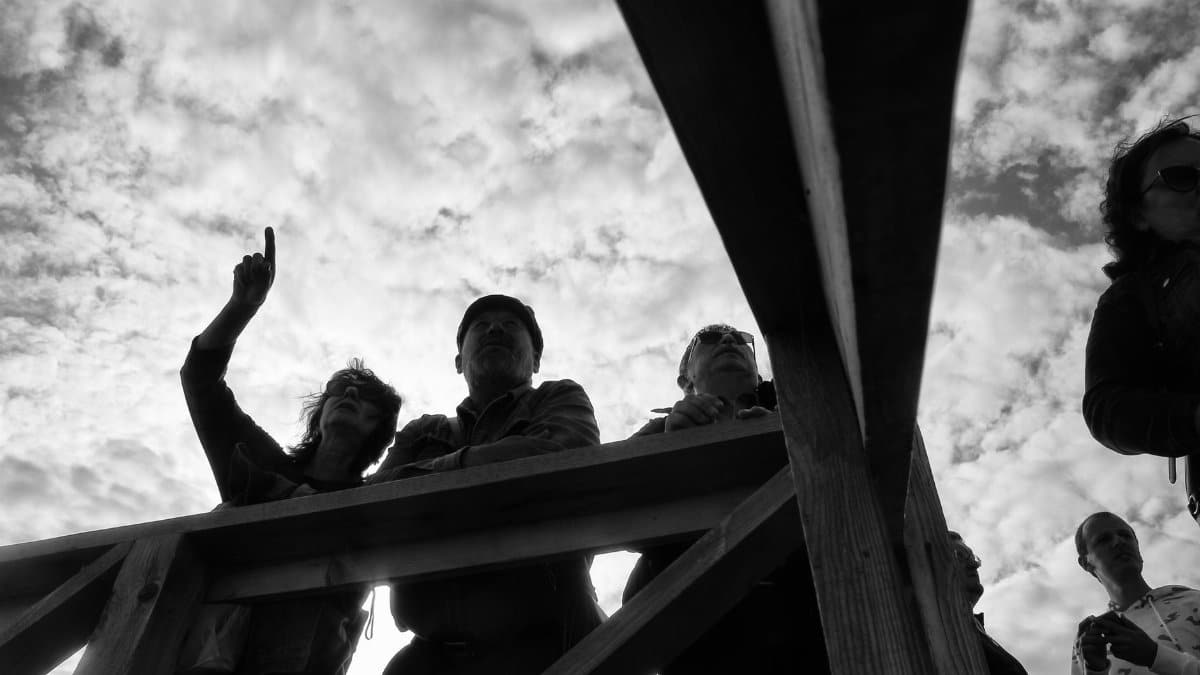 Low-angle view of people on a wooden railing silhouetted against a cloudy sky.