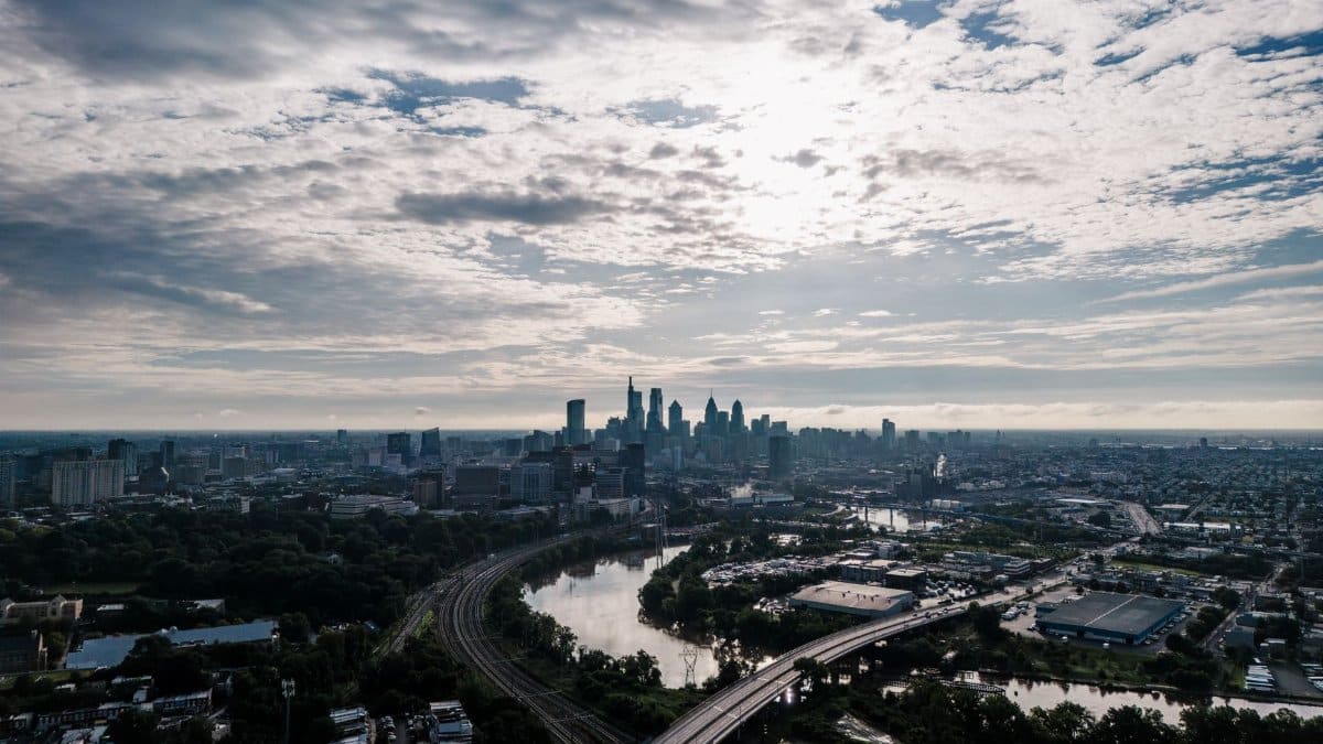 Stunning aerial view of Philadelphia's skyline featuring a river and cityscape under a cloud-filled sky.