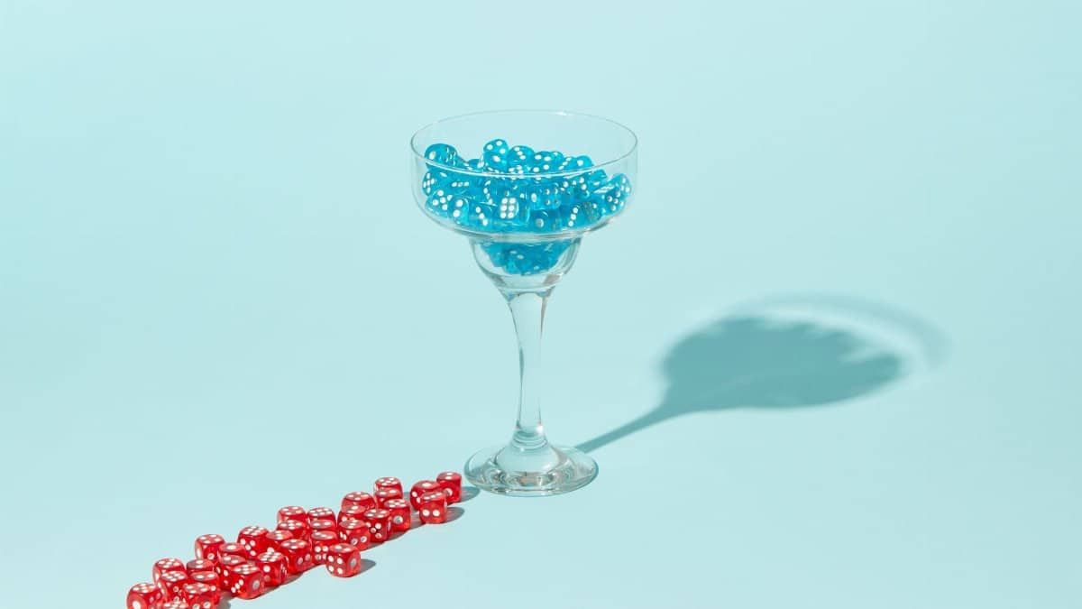 Artistic display of blue dice in a glass and scattered red dice on a pastel blue background.