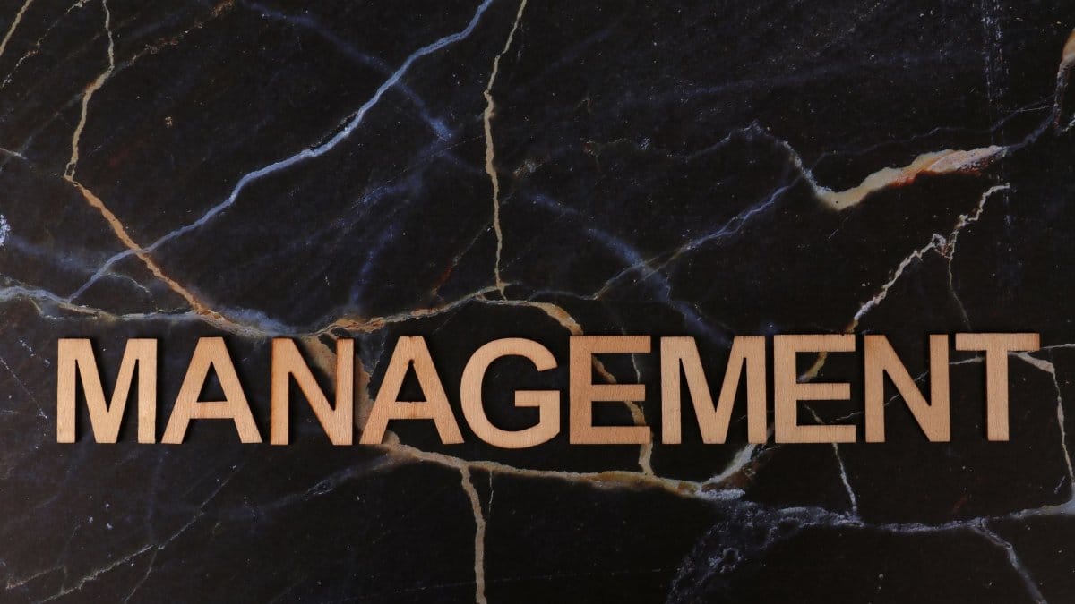 Wooden letters spelling 'Management' on black marble background with golden veins.