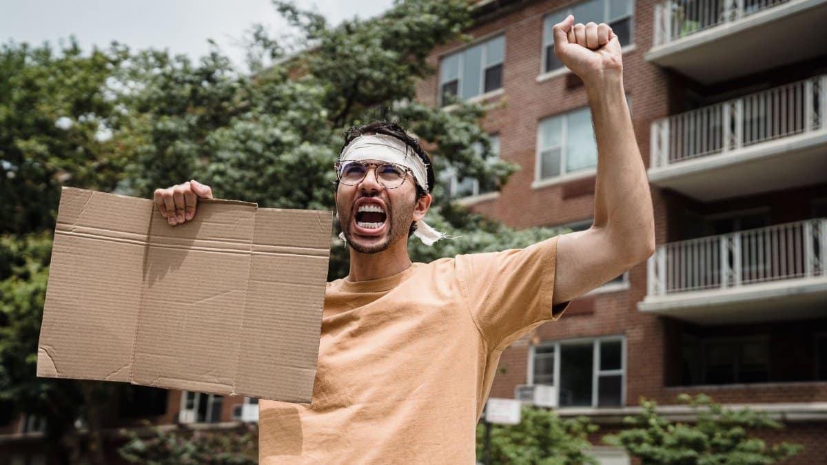 A man passionately protests with a blank cardboard sign outside apartment buildings.