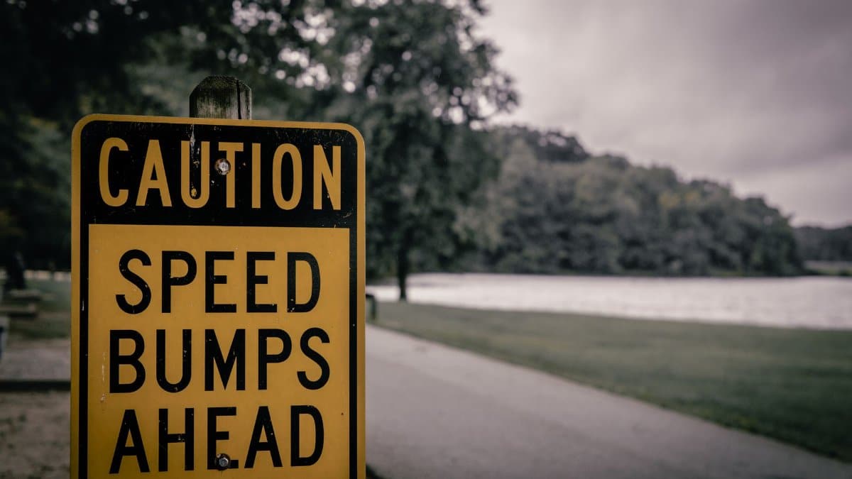 Yellow caution sign warning of speed bumps, placed in a park environment, overcast day.