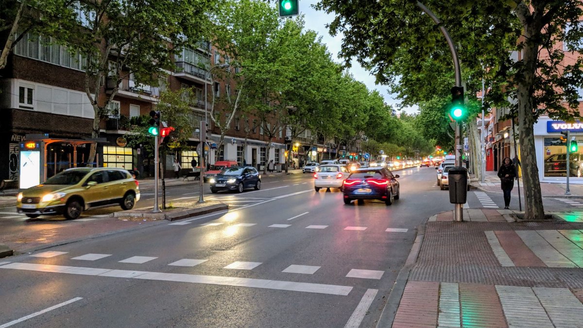 Bustling urban street in Madrid at dusk with cars, pedestrians, and green traffic lights.