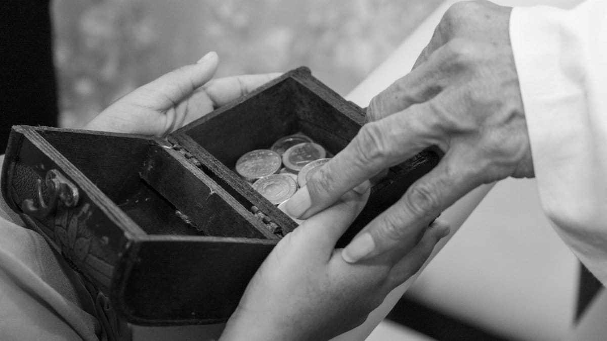 A touching black and white image of hands exchanging coins in a small wooden box, symbolizing trust and tradition.
