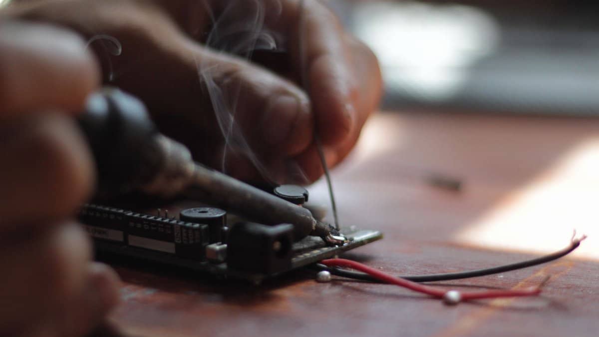 Detailed view of soldering process with visible smoke on an electronic circuit board, emphasizing precision.