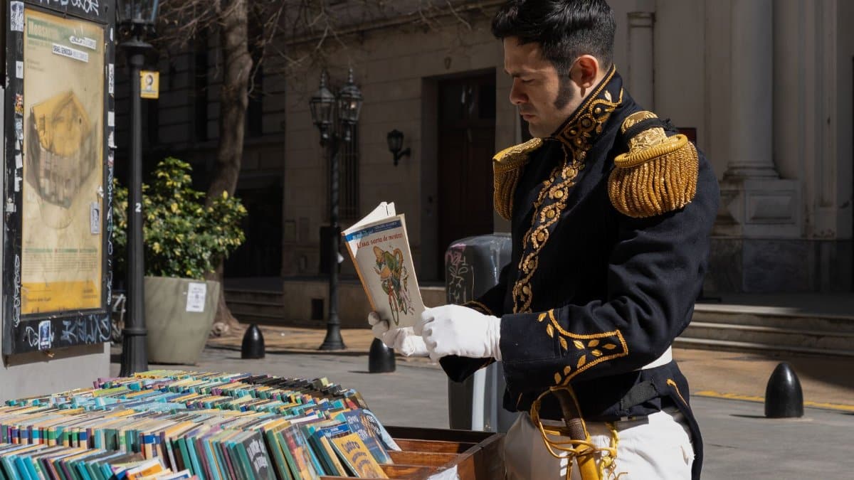 Man in historical military attire reading a book outdoors in Buenos Aires.