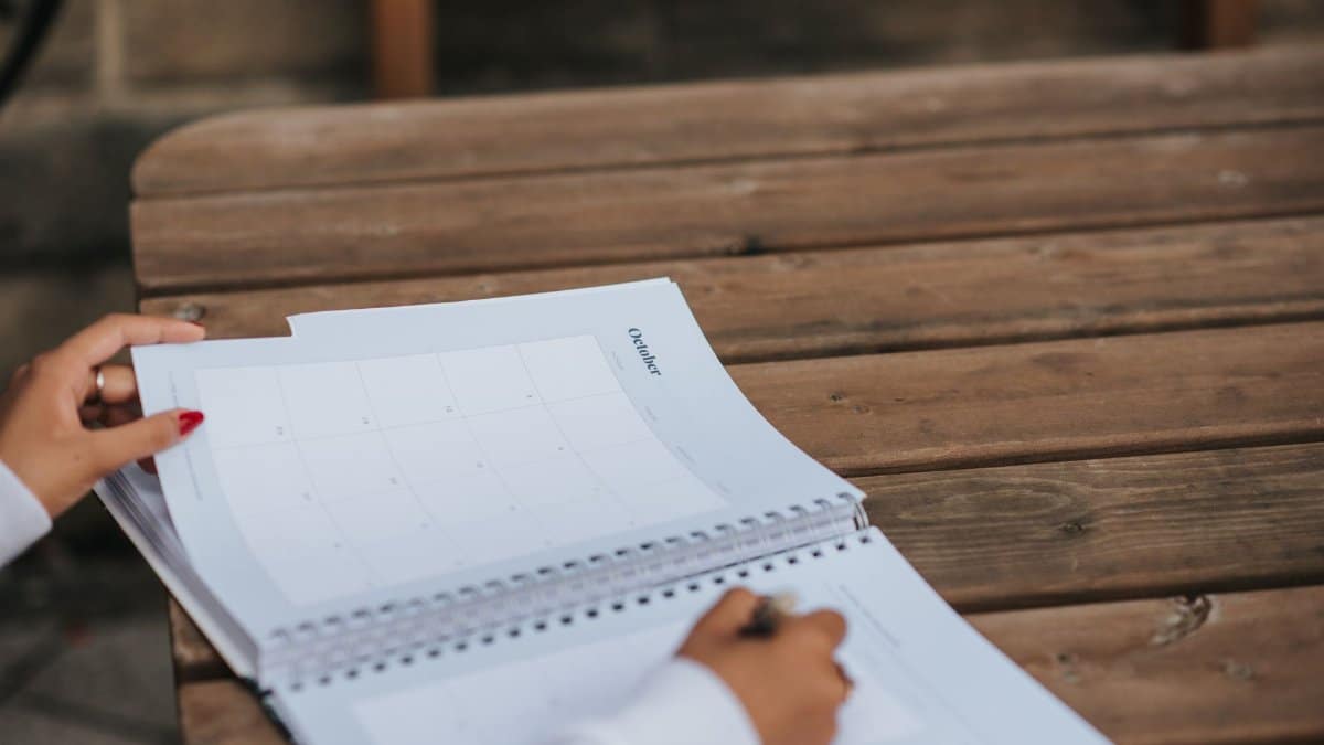 Crop anonymous female student writing in planner while sitting at wooden table in park