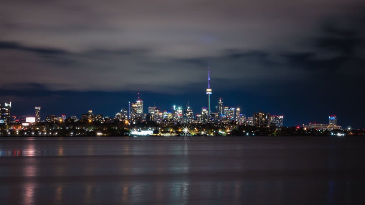Stunning view of Toronto's skyline with the illuminated CN Tower across the lake at night.