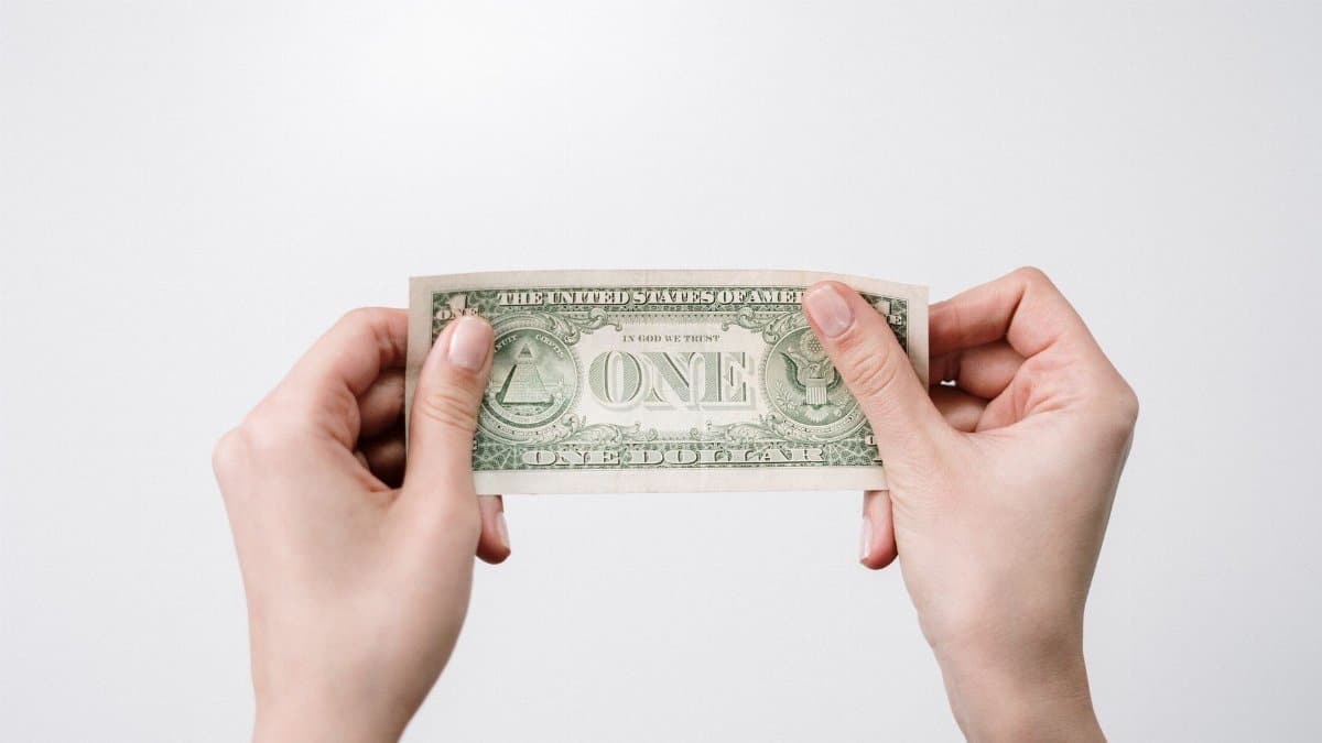 A close-up image of hands holding a one dollar bill, symbolizing finance and economy.