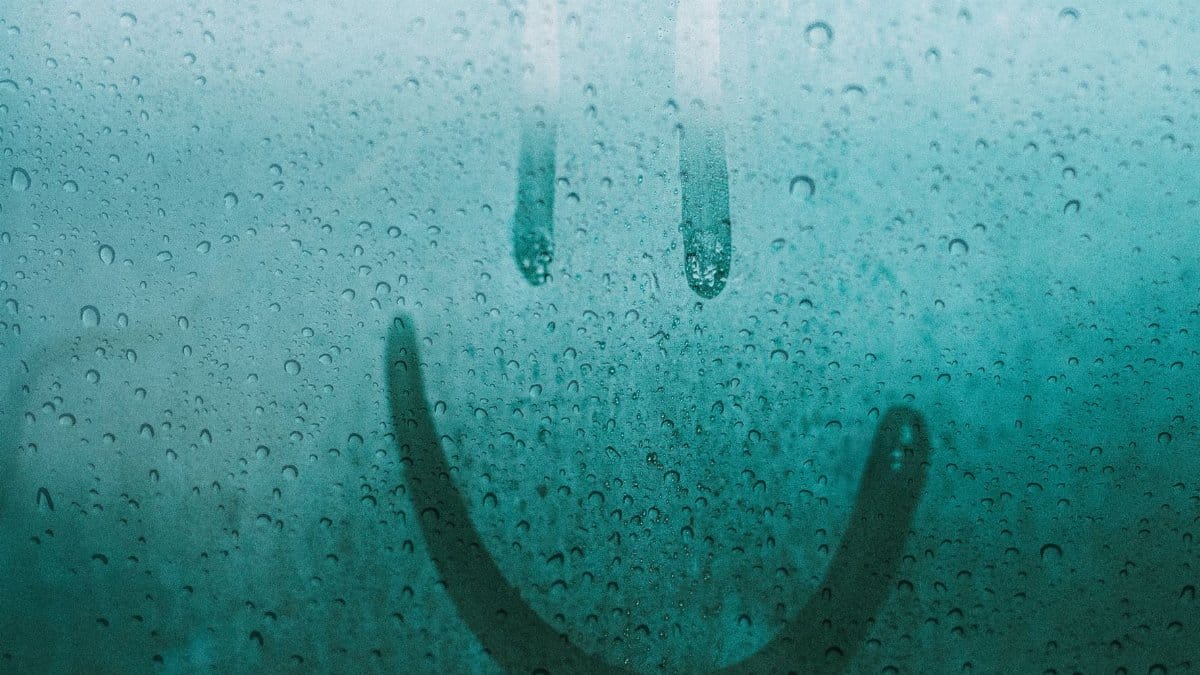 A smiley face drawn on a wet window, featuring water drops after the rain.