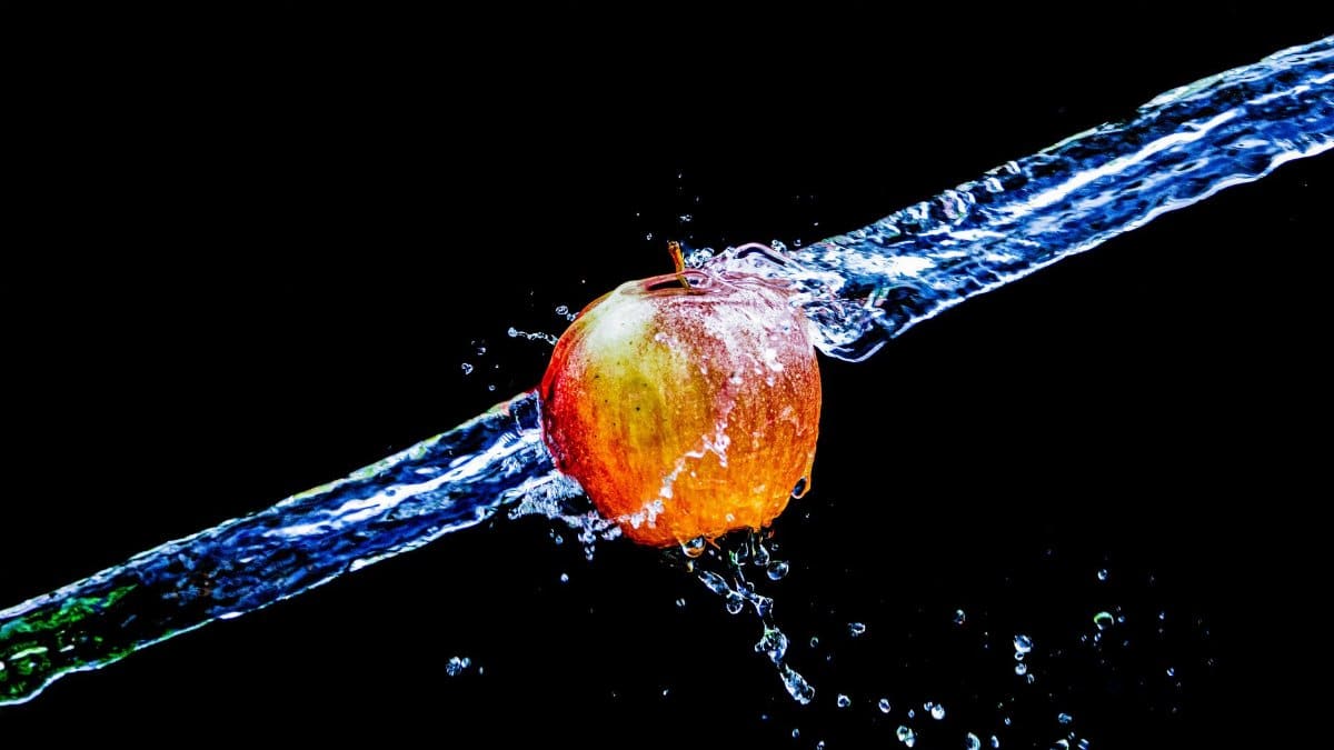 Vibrant apple captured amidst a dramatic water splash on a black background.