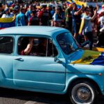 A vibrant Venezuelan community parade in Buenos Aires featuring a classic car and national flags waving.
