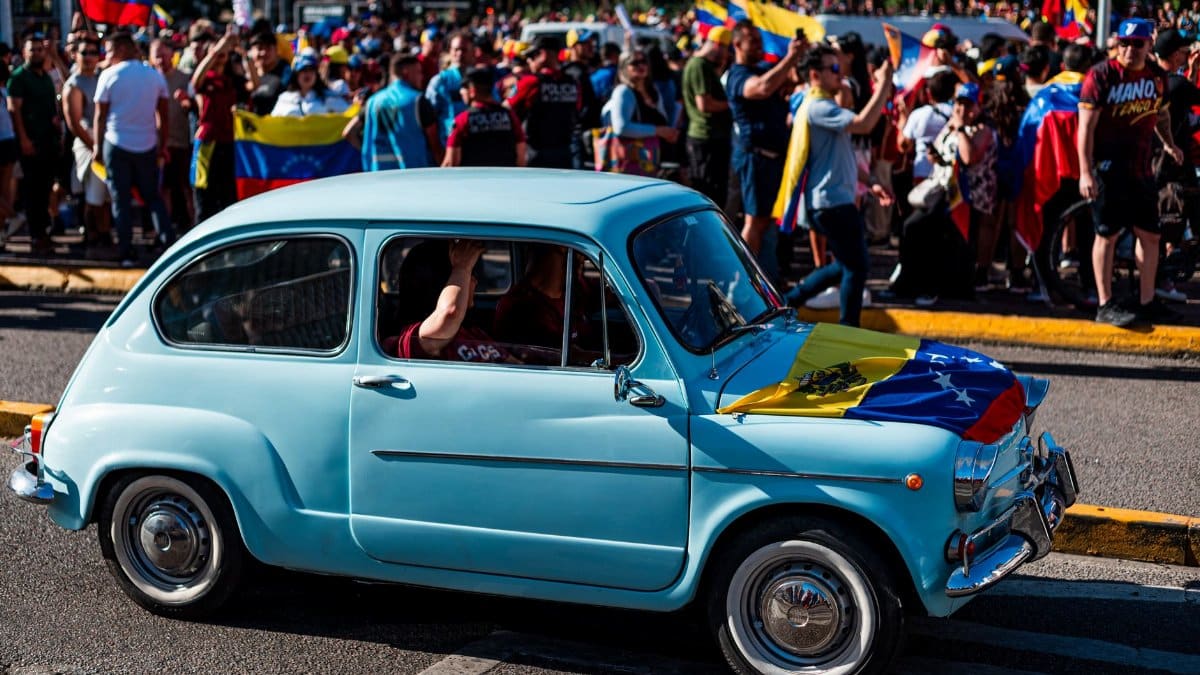 A vibrant Venezuelan community parade in Buenos Aires featuring a classic car and national flags waving.