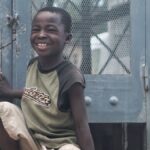 Happy child in Haiti smiles brightly while sitting outdoors.