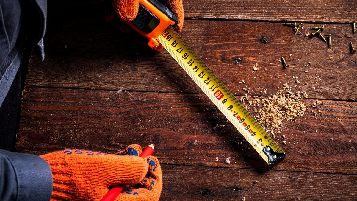 Close-up of gloved hands using a tape measure on wooden surface for precise carpentry.