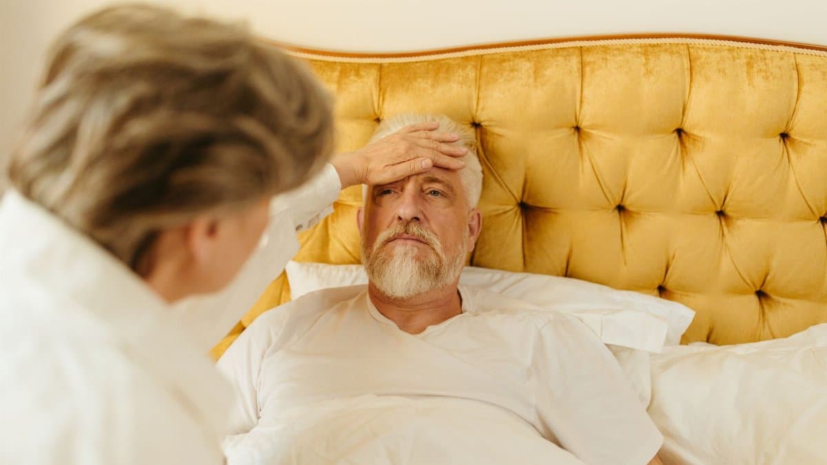 Elderly man in bed receiving care from a woman at home.