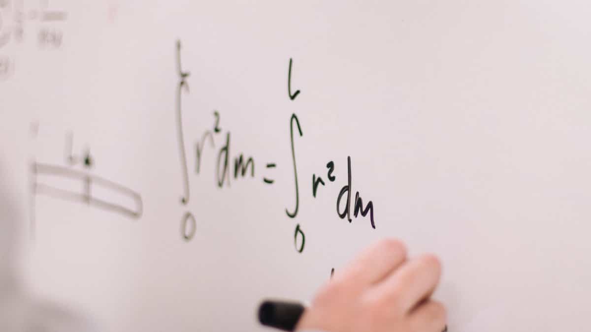 Person writing math equations on a whiteboard, focusing on integrals and formulas.