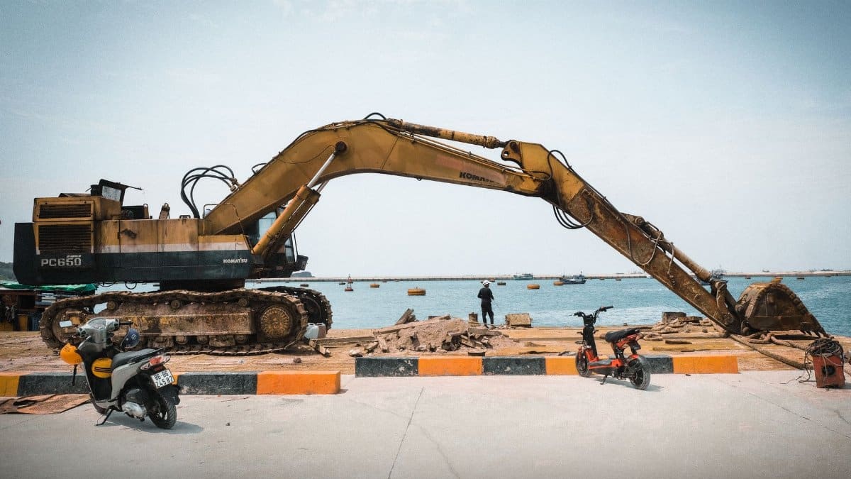 A large excavator working on a coastal construction site with a sea view.