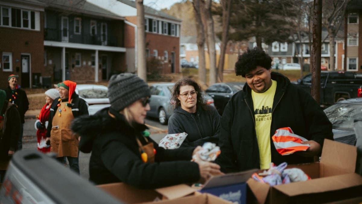 Volunteers gather to distribute wrapped Christmas gifts to the community in a neighborhood setting.