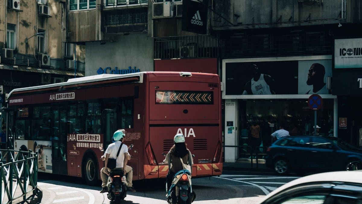 Dynamic street view capturing two scooter riders trailing a bus in bustling Macau city.