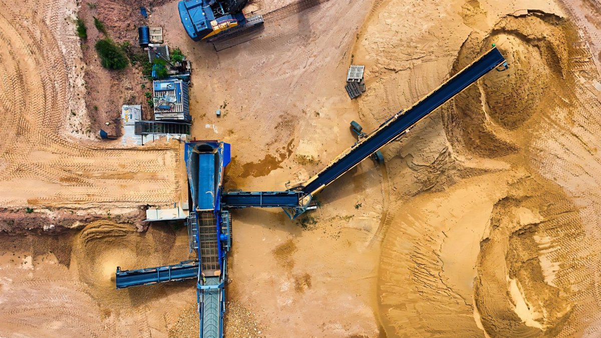 Top view of sand mining machinery and piles in outdoor quarry.