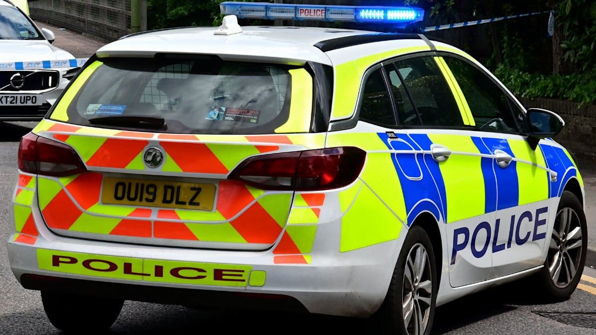 Back view of a British police car with flashing blue lights on a city road, ensuring law enforcement.