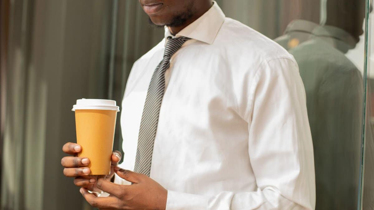 Professional man holding a disposable coffee cup in a modern office setting.