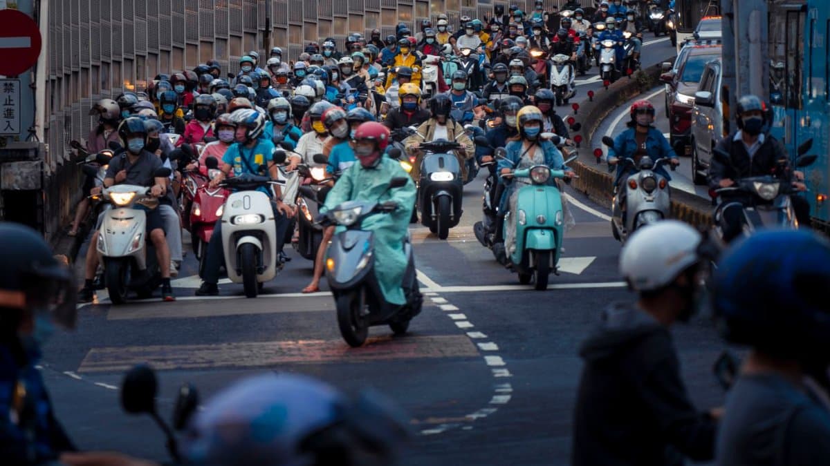 A crowded city street with numerous scooters and riders during rush hour traffic.