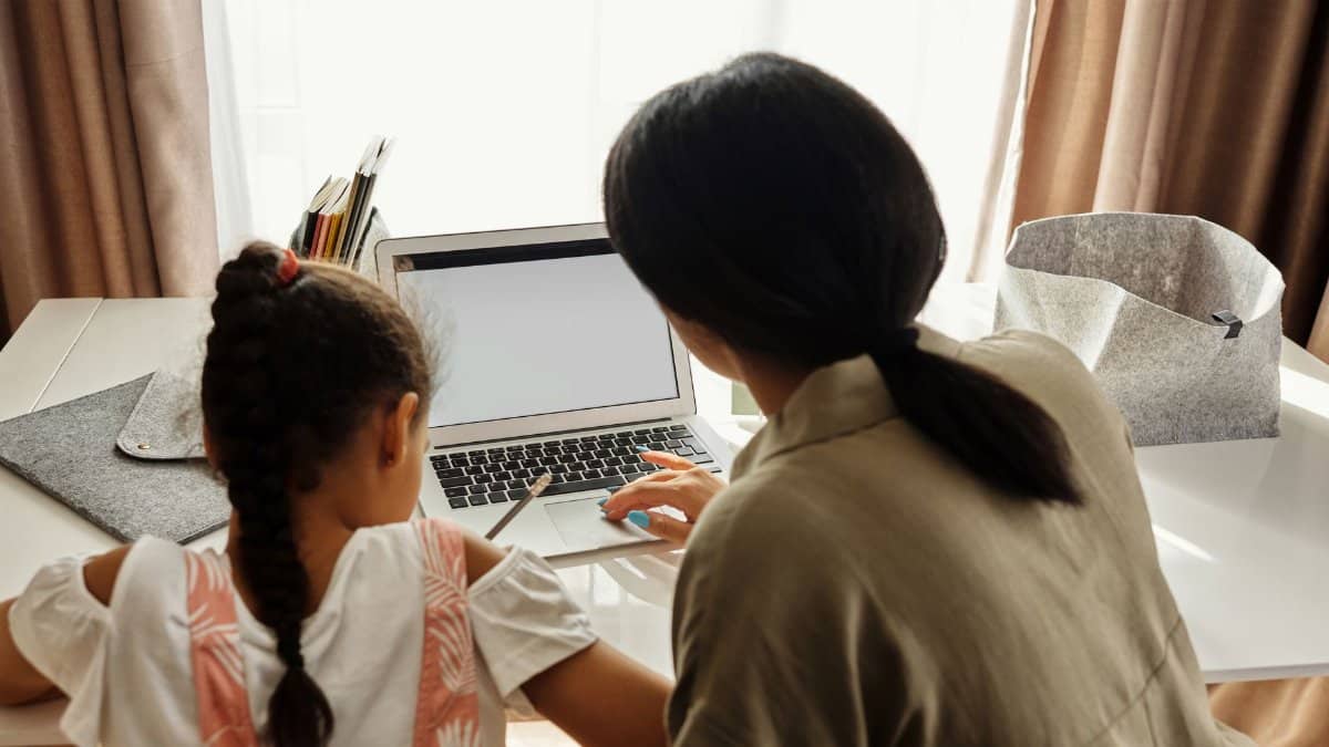 A mother helps her daughter with online learning on a laptop at home, emphasizing family education.