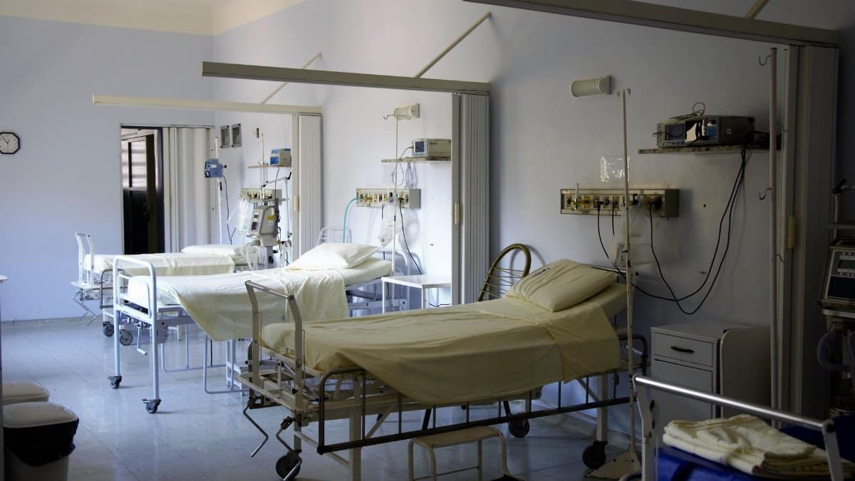 Spacious hospital room with several empty beds and medical equipment, emphasizing healthcare and hygiene.